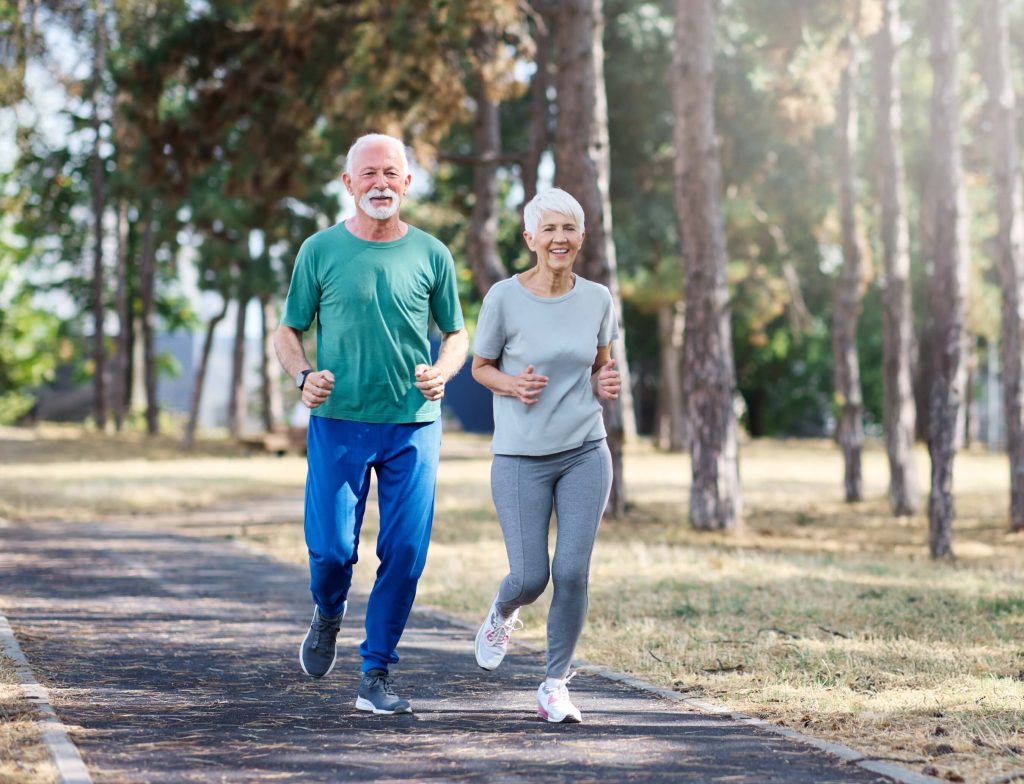 Smiling older couple jogging together on a tree-lined park path